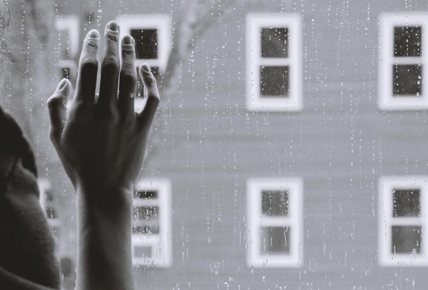 Mano di una donna appoggiata al vetro di una finestra bagnato dalla pioggia