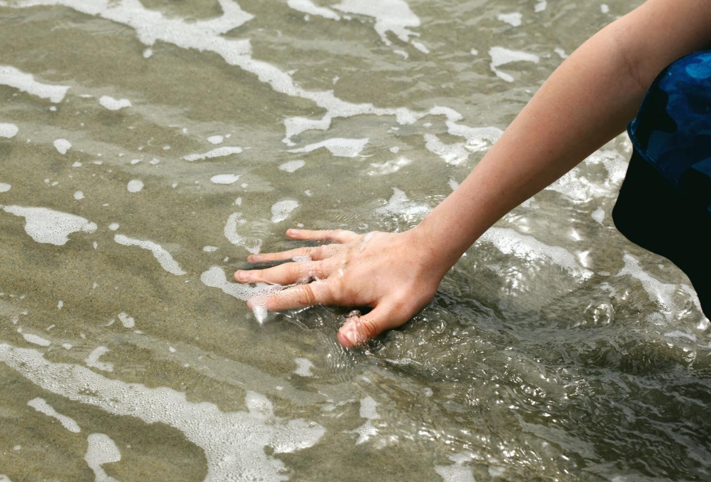 una mano tocca l'acqua del mare